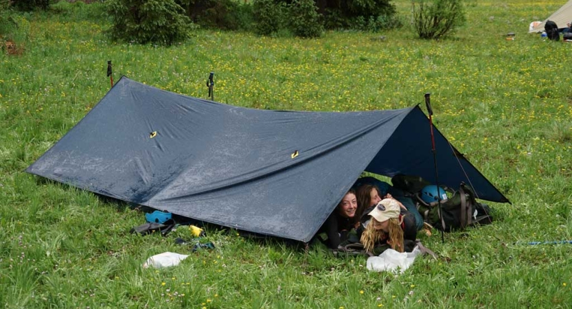 Students smile from under a tarp shelter